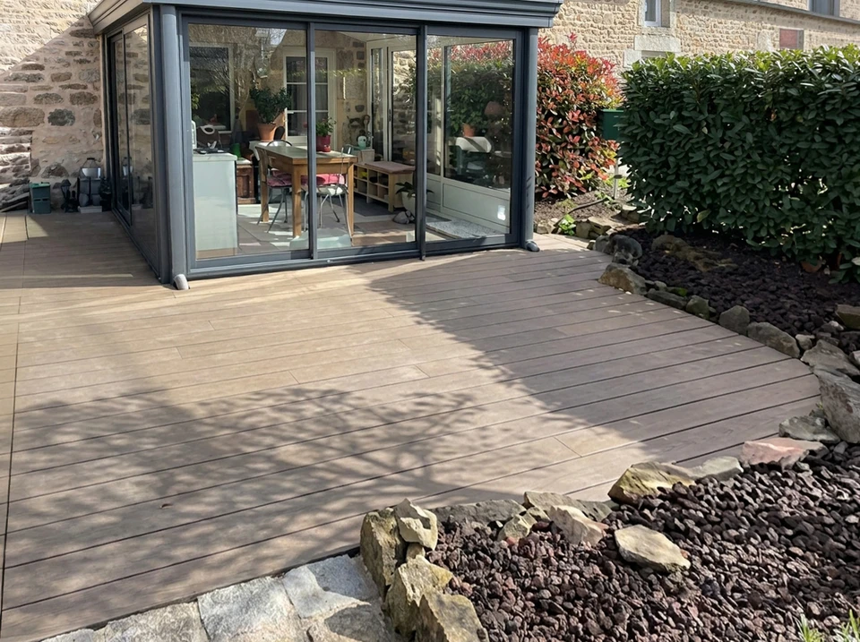 Terrasse extérieure aménagée avec salon de jardin en résine tressée, parasol vert lime, table ronde métallique et barbecue