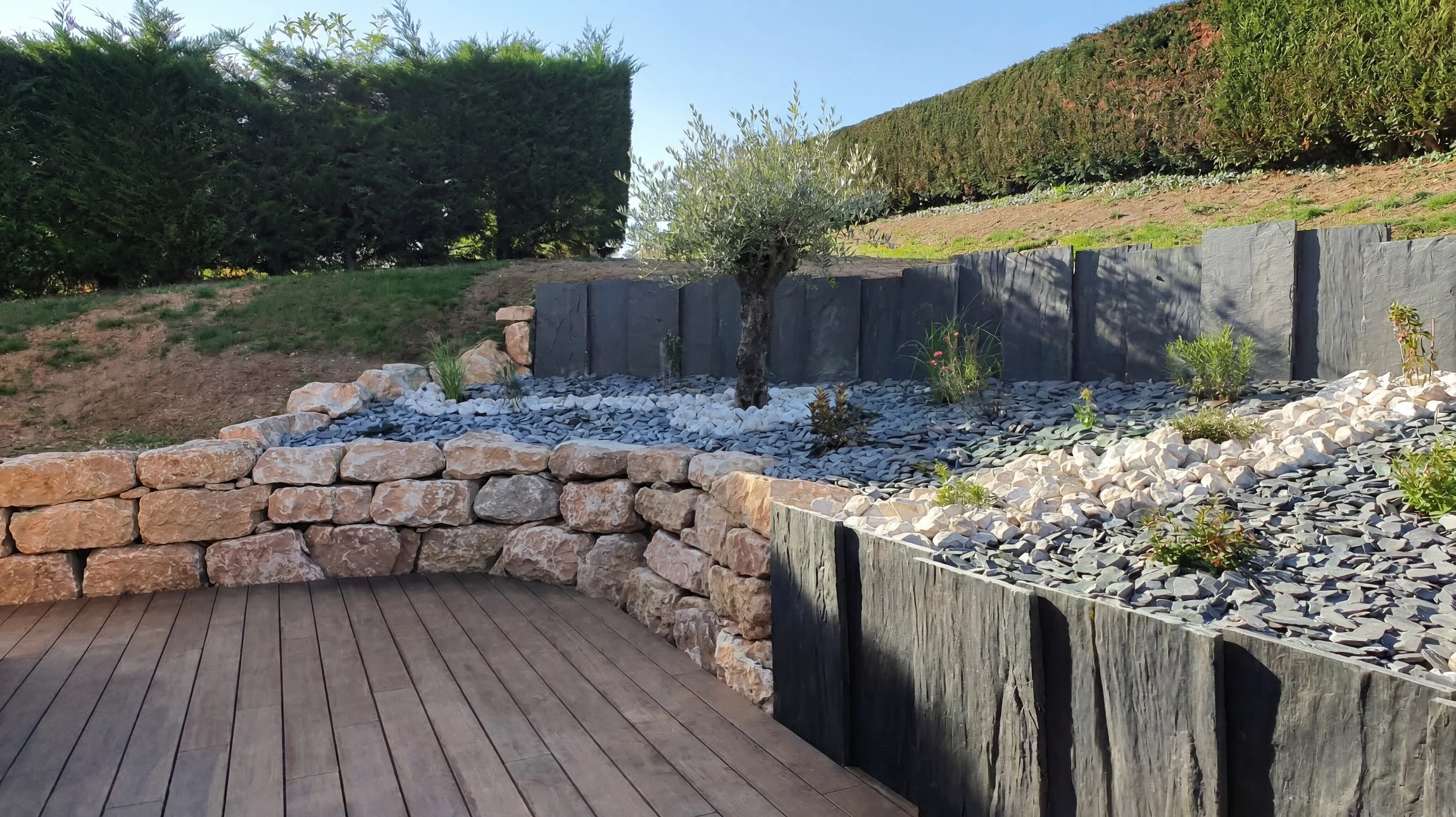 Terrasse extérieure aménagée avec mobilier de jardin en bois teck, parasol déporté beige, jardinière verticale en palettes recyclées avec pots colorés suspendus, brise-vue bambou, chaise pliante, tabouret noir